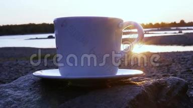 一杯带烟的红茶，站在河边的一块岩石上，看着金色的夕阳，在水面上闪闪发光。 <strong>高清高清</strong>